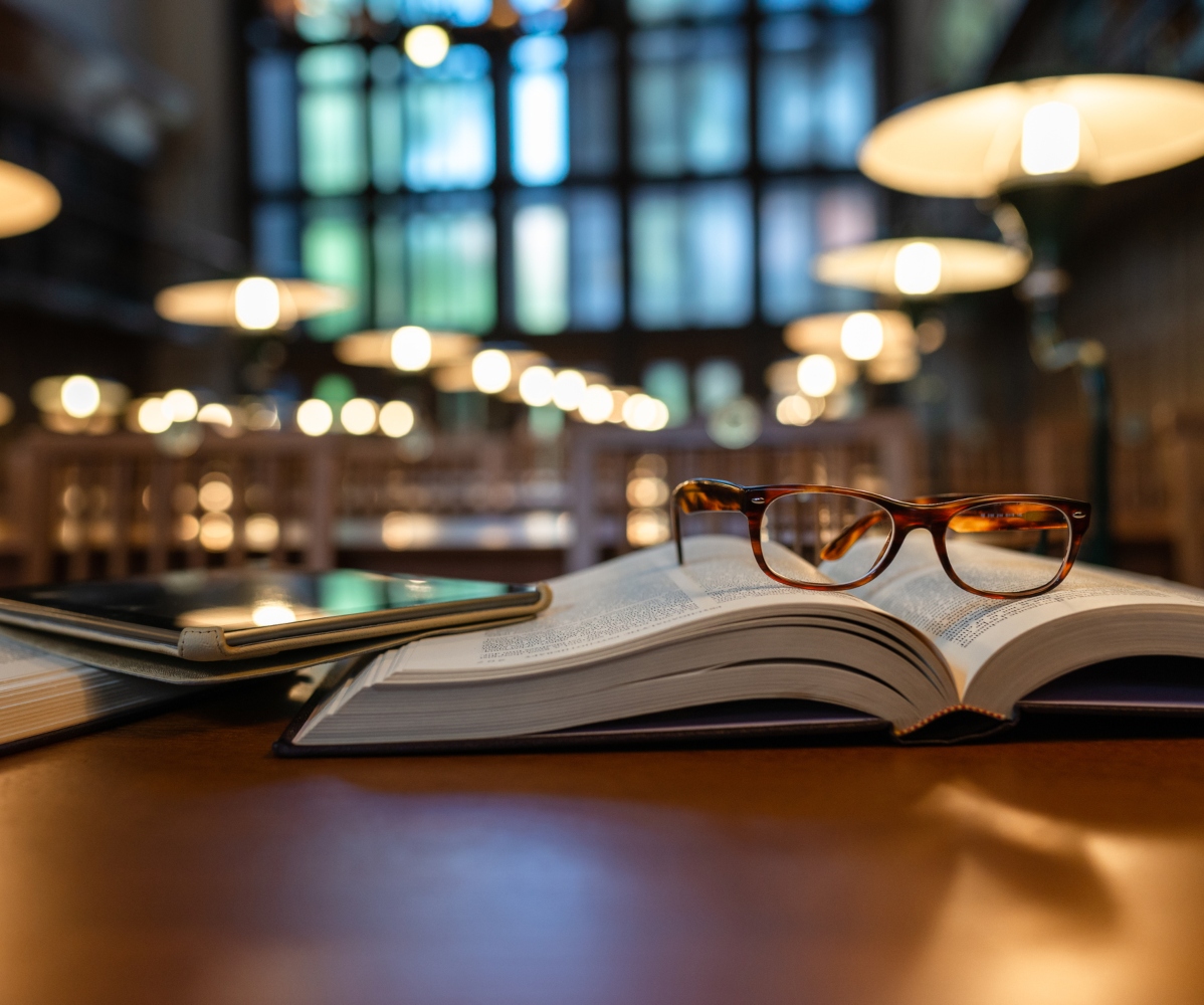 óculos pousados em cima de livro aberto numa biblioteca