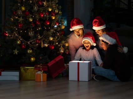 família a abrir prendas junto à árvore de Natal