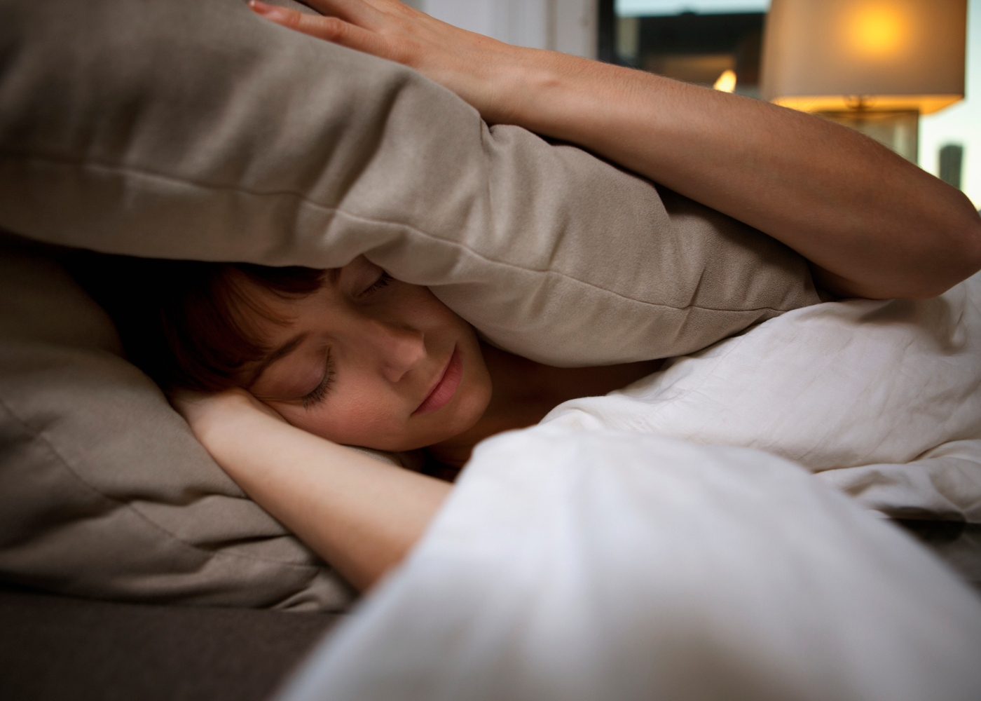 mulher a tentar dormir com almofada a tapar ouvidos