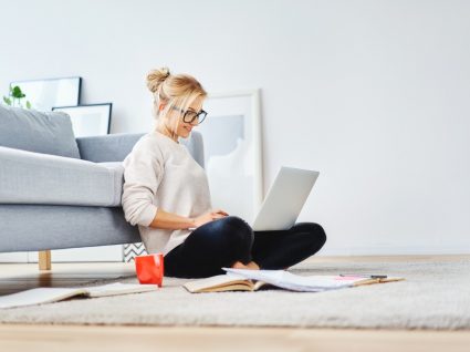 mulher sentada no chão encostada ao sofá a trabalhar no computador