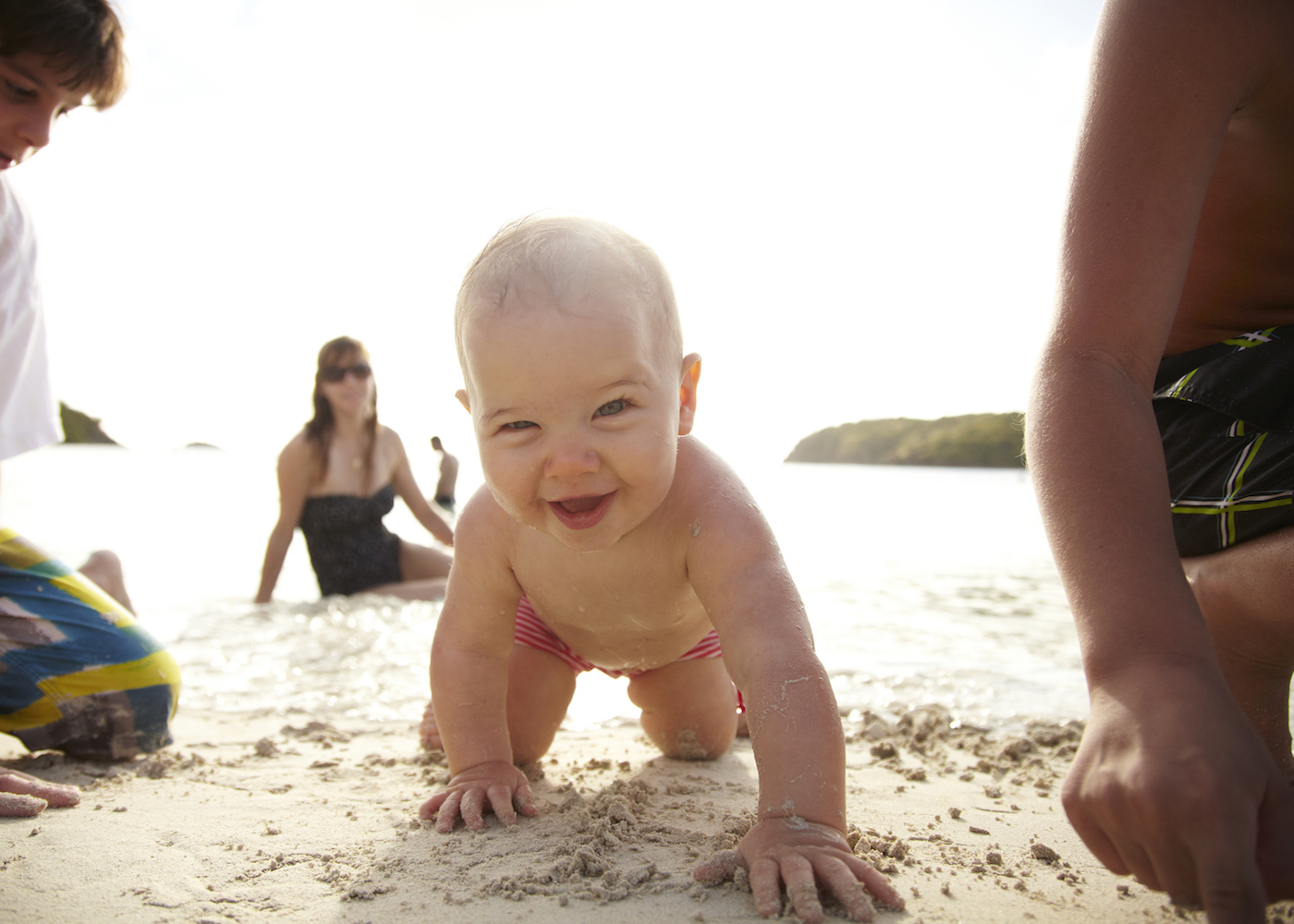 bebé a sorrir na areia da praia com familiares