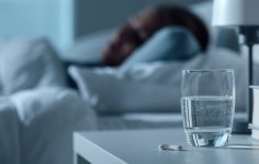 mulher na cama com copo de água e comprimidos para dormir