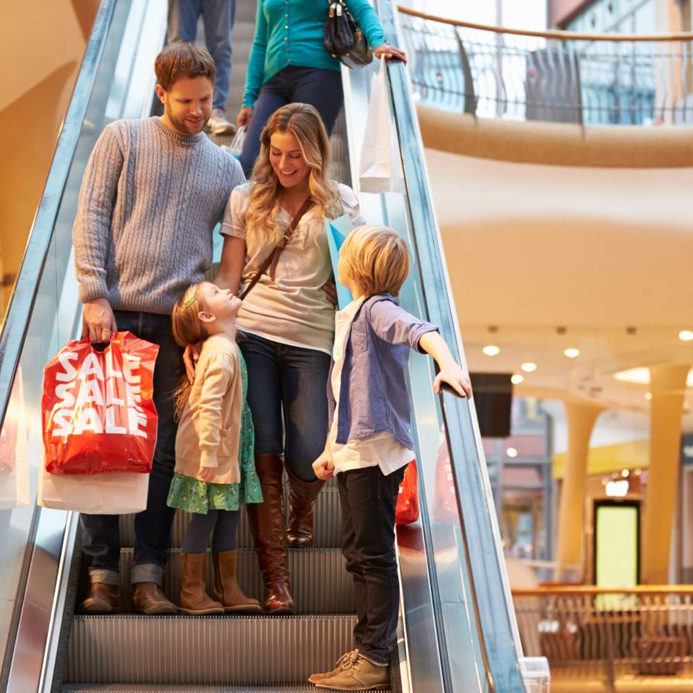 família com sacos de compras a descer a escada rolante de um centro comercial 
